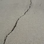 A large crack in a concrete floor down the image from top to bottom that is in need of MKZ's concrete floor repair service.