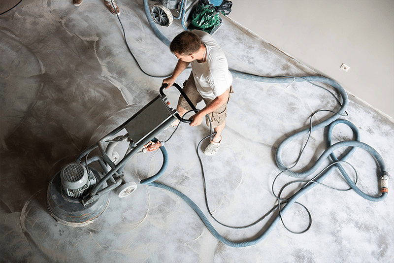 Top down photo of a worker smoothing down a concrete floor with a grinding machine