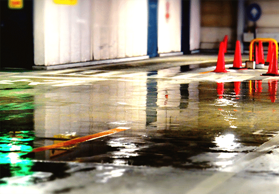 A photo of an indoor carpark showing a huge puddle forming on the concrete floor.